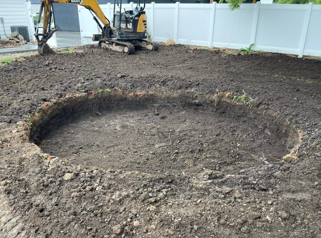 Image showing a hole excavated for an in-ground trampoline. There is an excavator in the background.